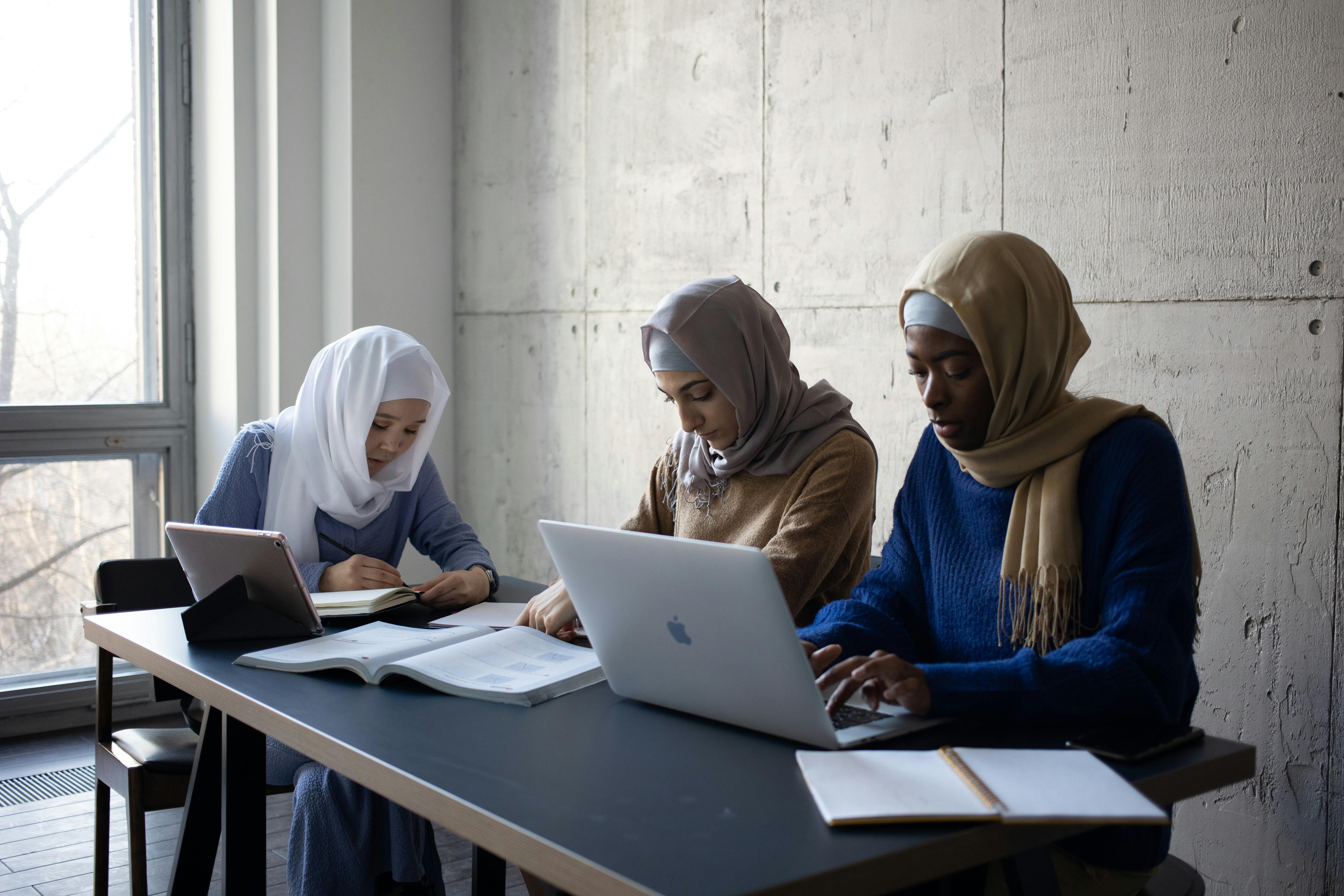 Studentesse con il velo che studiano insieme su libri, tablet e macbook